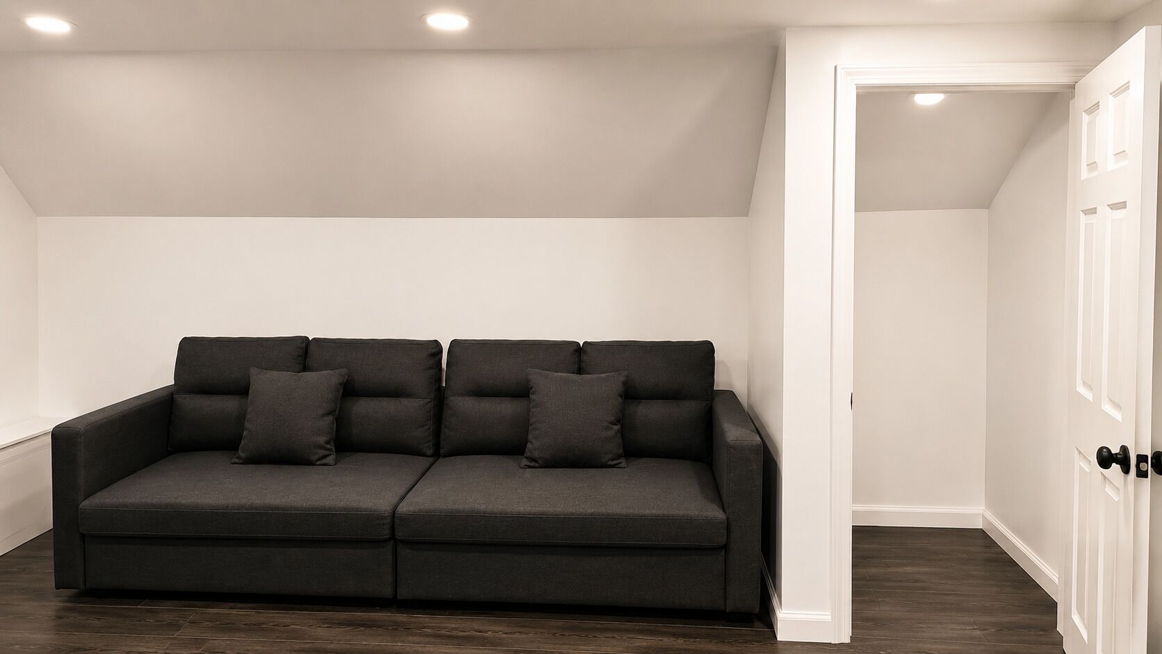 A dark grey sofa with cushions in a room with white walls and wooden flooring.