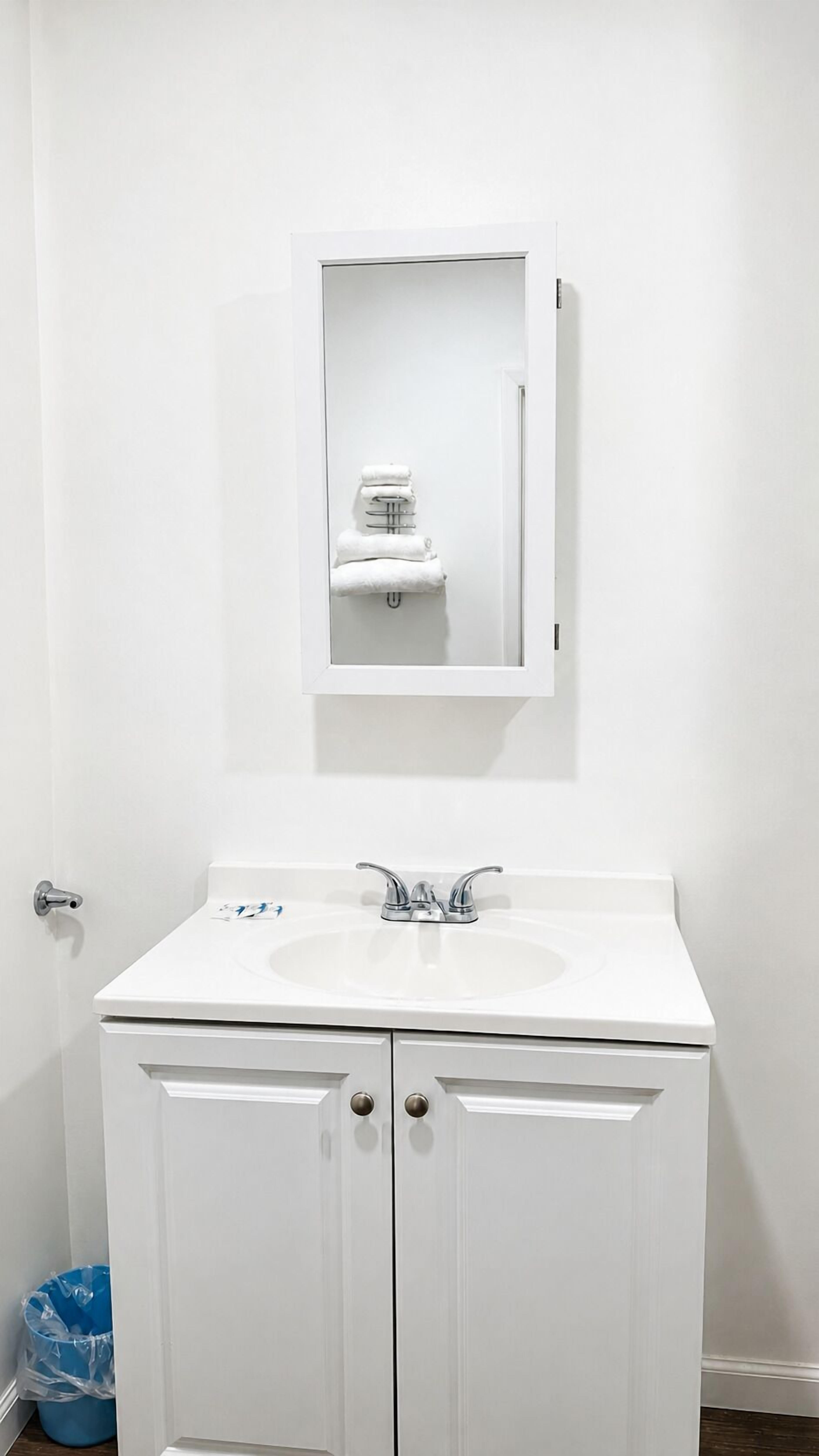 Un baño blanco con lavamanos, espejo y toallero.
