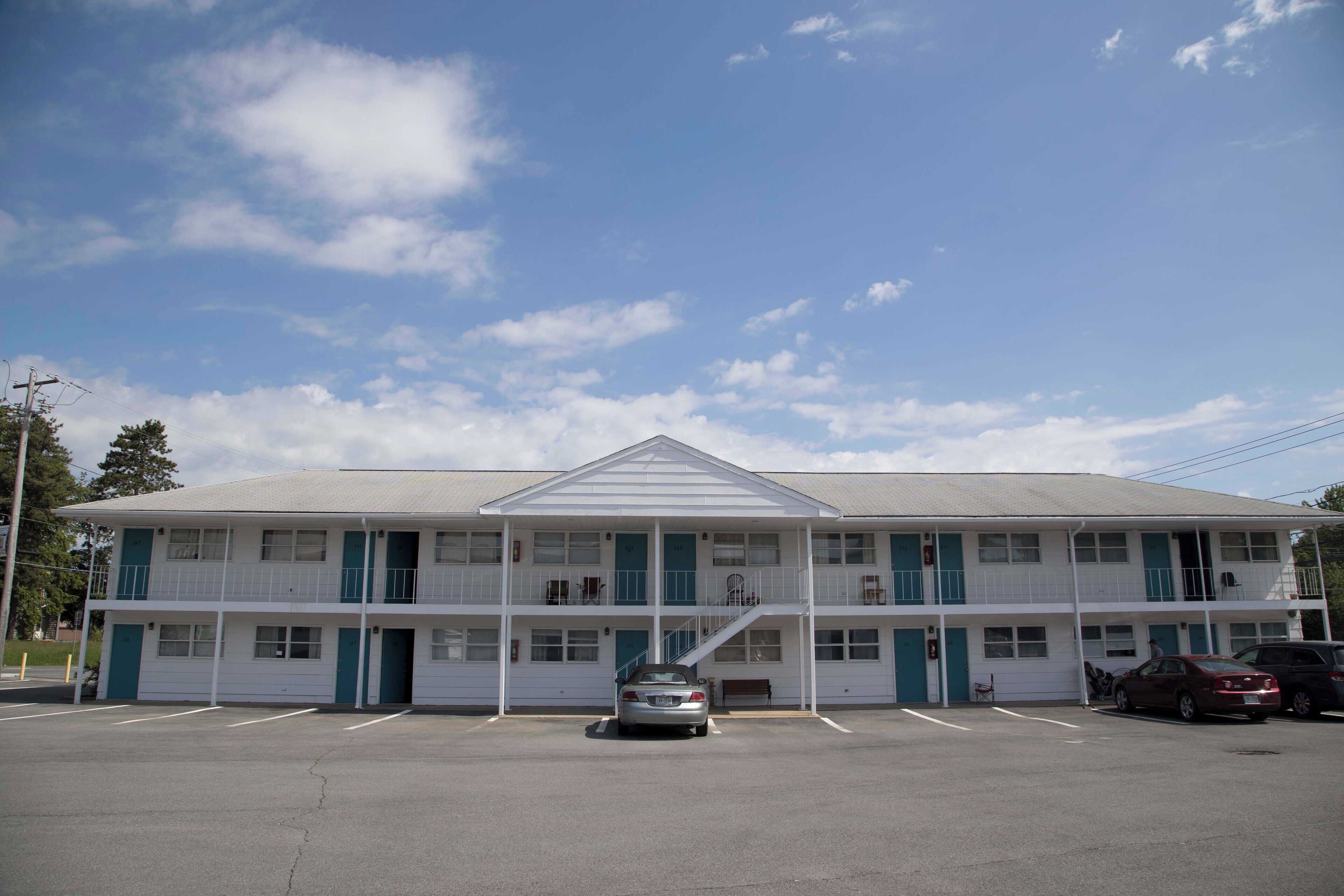 A two-story motel with a central staircase, a parking lot, and a clear sky.