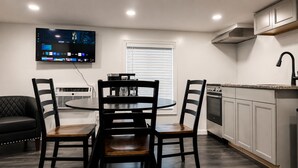 A modern kitchen with a dining area, a flat-screen TV mounted above the table, and a built-in oven. - Lake George Residence LLC (South Glens Falls)
