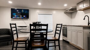 A modern kitchen with a dining area, a flat-screen TV mounted above the table, and a built-in oven. - Lake George Residence LLC (South Glens Falls)