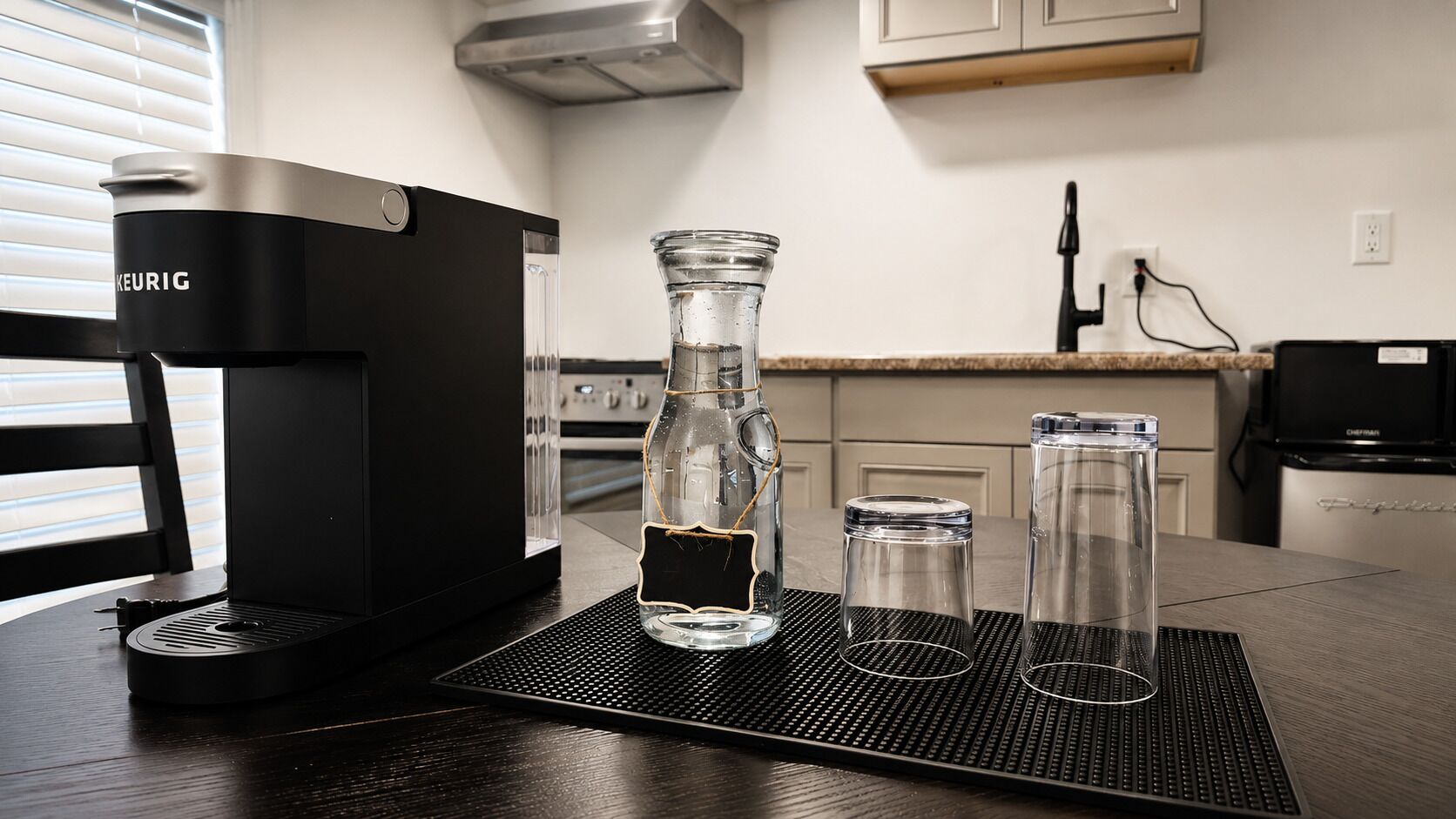 Una cafetera, una botella de vidrio y dos recipientes de vidrio sobre una mesa en una cocina.