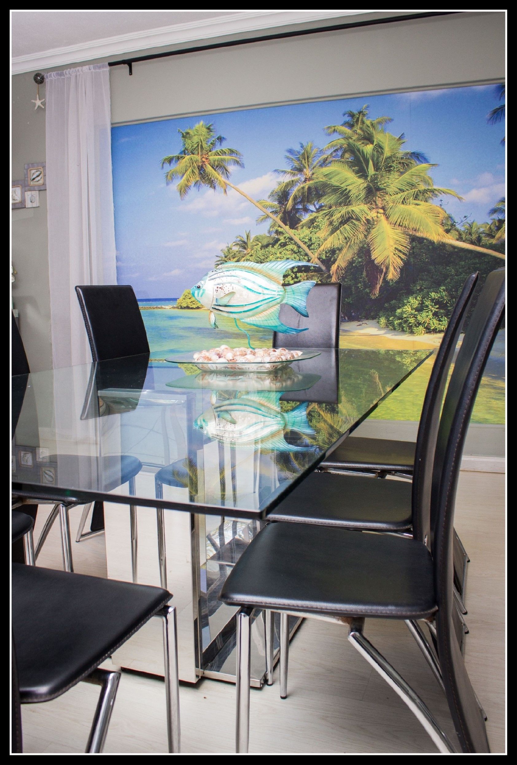 Uma área de refeições com mesa e cadeiras de vidro, um mural tropical na parede e uma decoração em forma de estrela no teto.