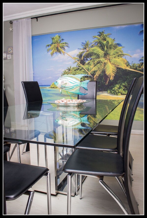 Uma área de refeições com mesa e cadeiras de vidro, um mural tropical na parede e uma decoração em forma de estrela no teto.