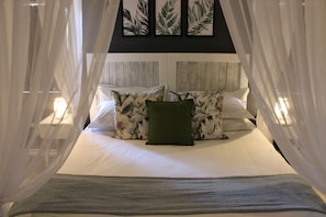 Ein Bett mit Baldachin, weißer Bettwäsche und einem grünen Kopfkissen.