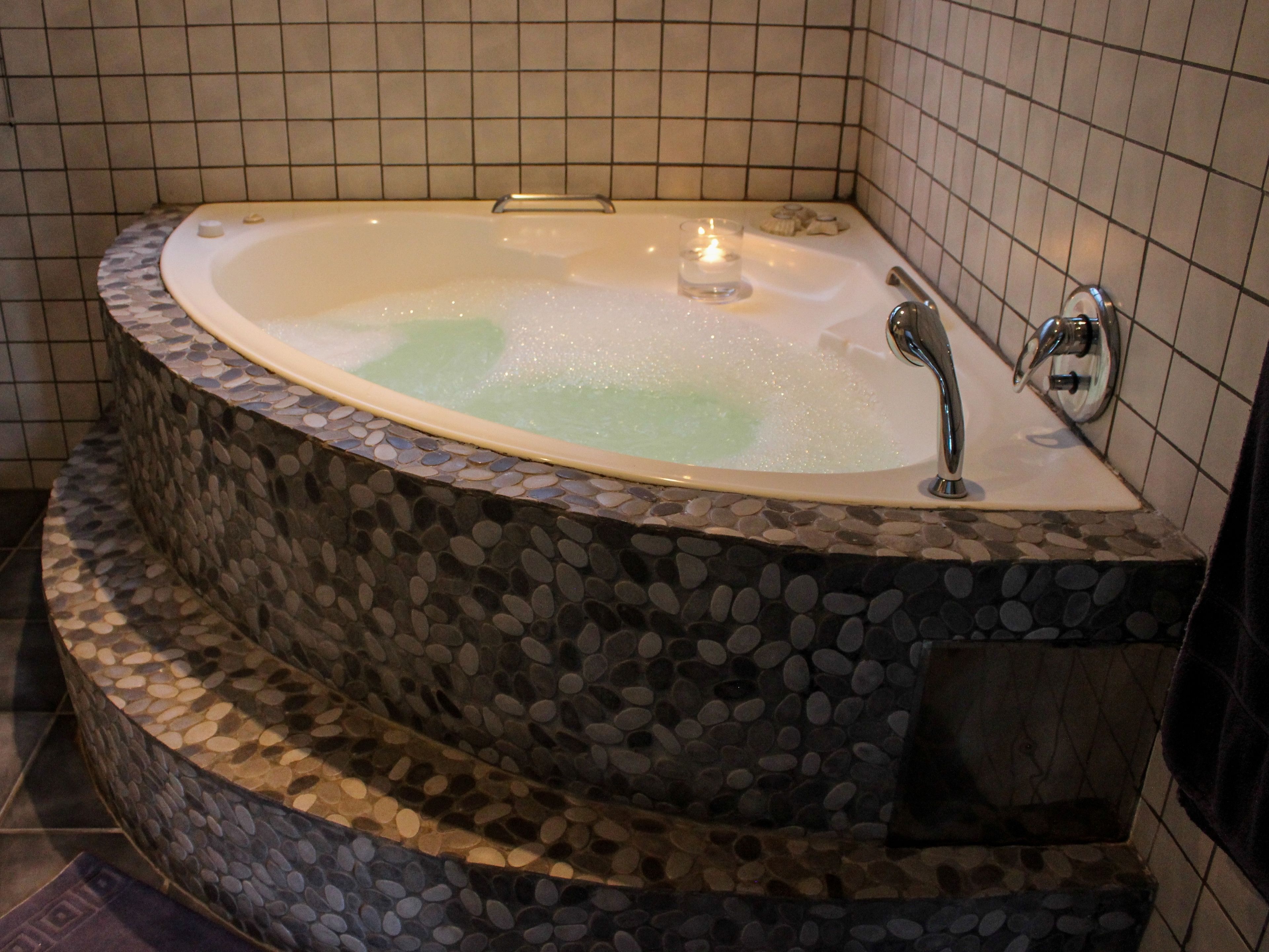 A modern bathroom with a freestanding bathtub, tiled walls, and a pebble-textured surround.