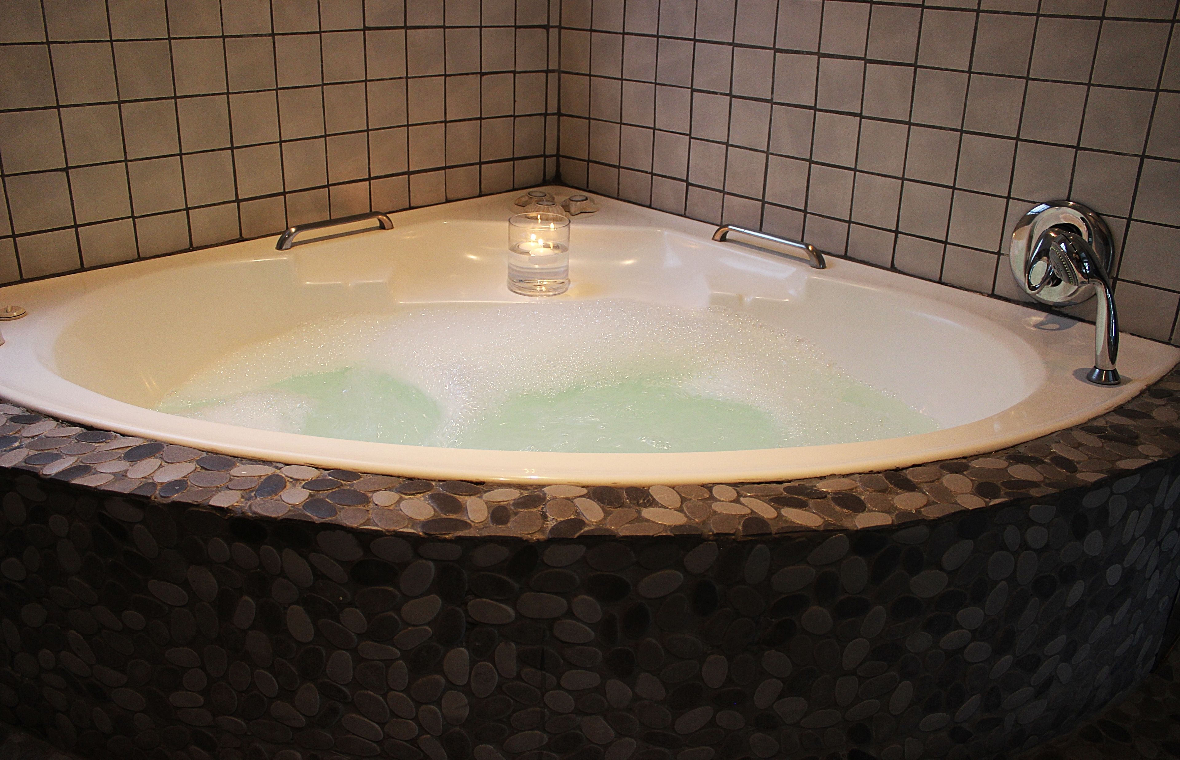 Eine Badewanne mit Mosaikverkleidung, ein Glaslicht und ein Wasserhahn.