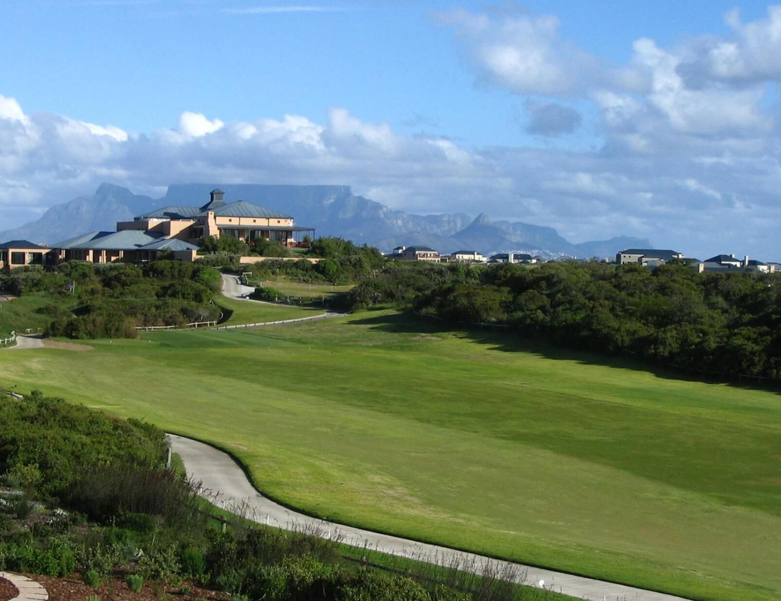 A golf course with a clubhouse, surrounded by lush greenery and mountains in the background.