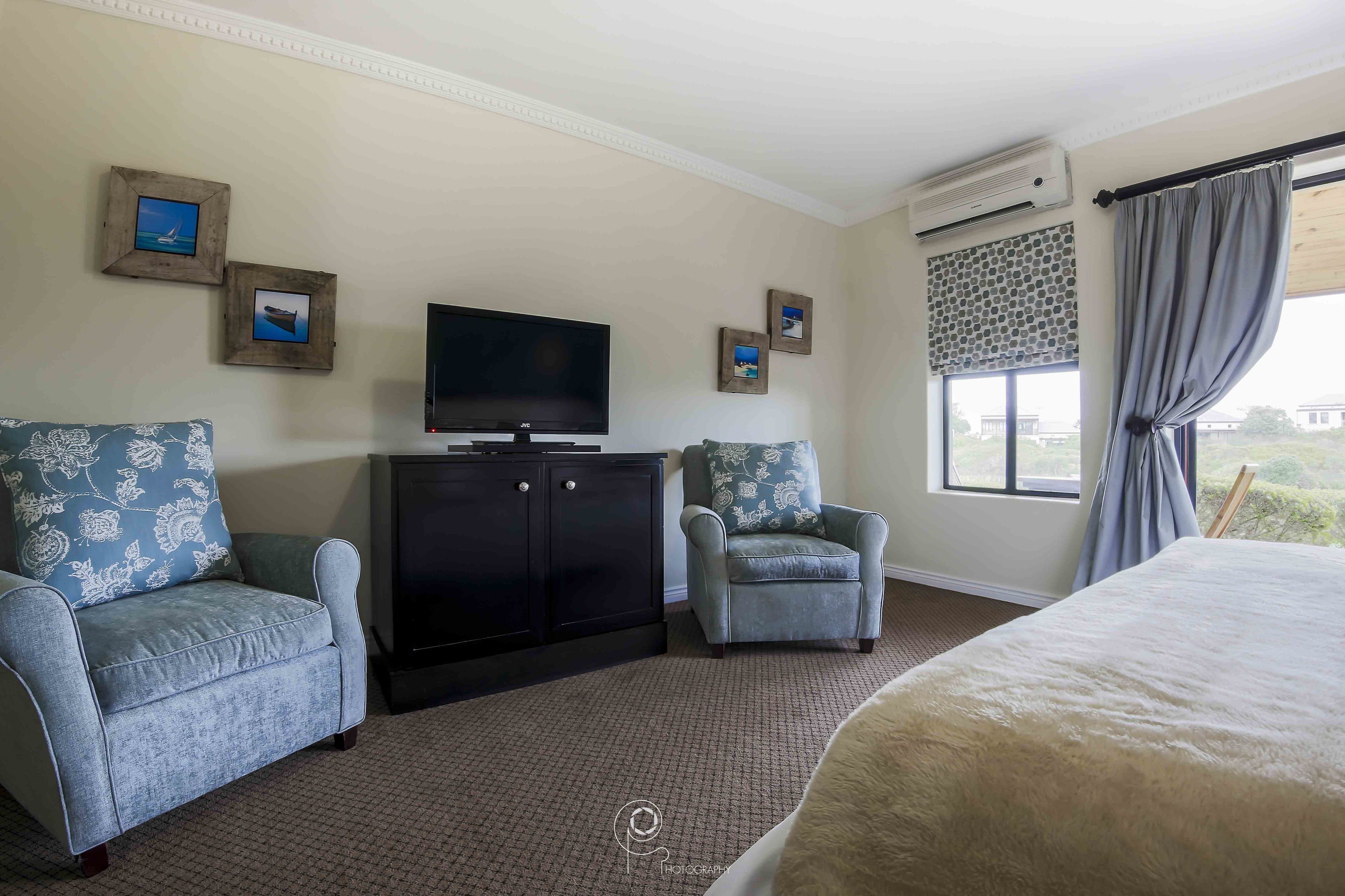 Une chambre d’hôtel avec un grand lit, deux fauteuils, une télévision, une armoire et une fenêtre avec des rideaux.