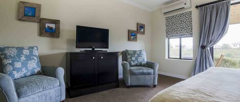 A hotel room with a large bed, two armchairs, a TV, a cabinet, and a window with curtains.