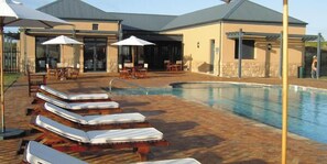 A pool area with lounge chairs and umbrellas, a covered seating area, and a building with a stone facade.