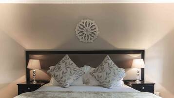 Una cama bien hecha con un cabecero decorativo, dos mesitas de noche con lámparas y un adorno en la pared.