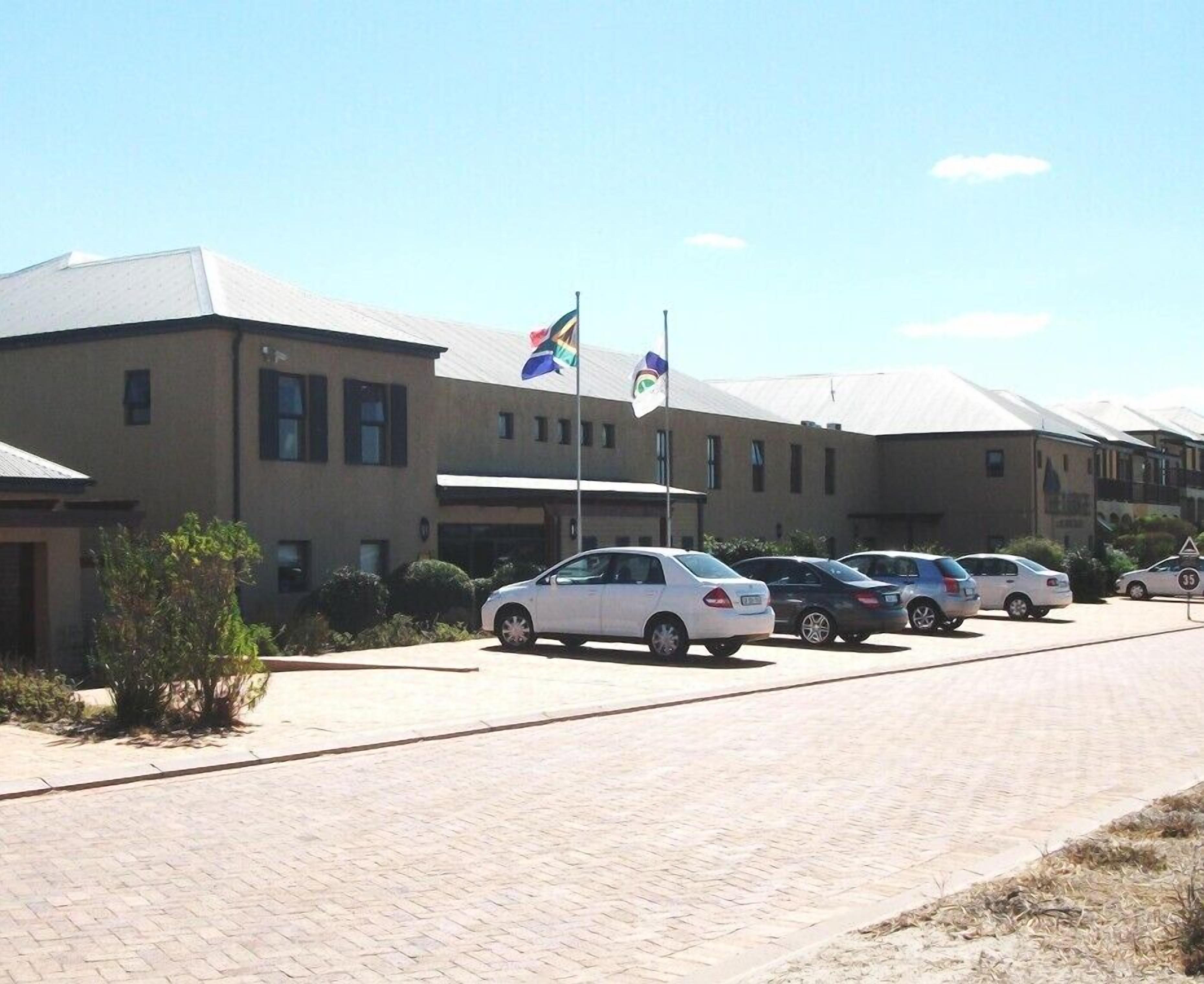 A parking lot with several cars, a building with multiple windows, and flags on a flagpole.