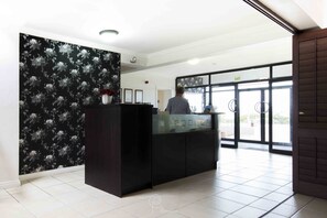 A reception area with a black counter, a floral wallpaper, and a glass door leading outside.