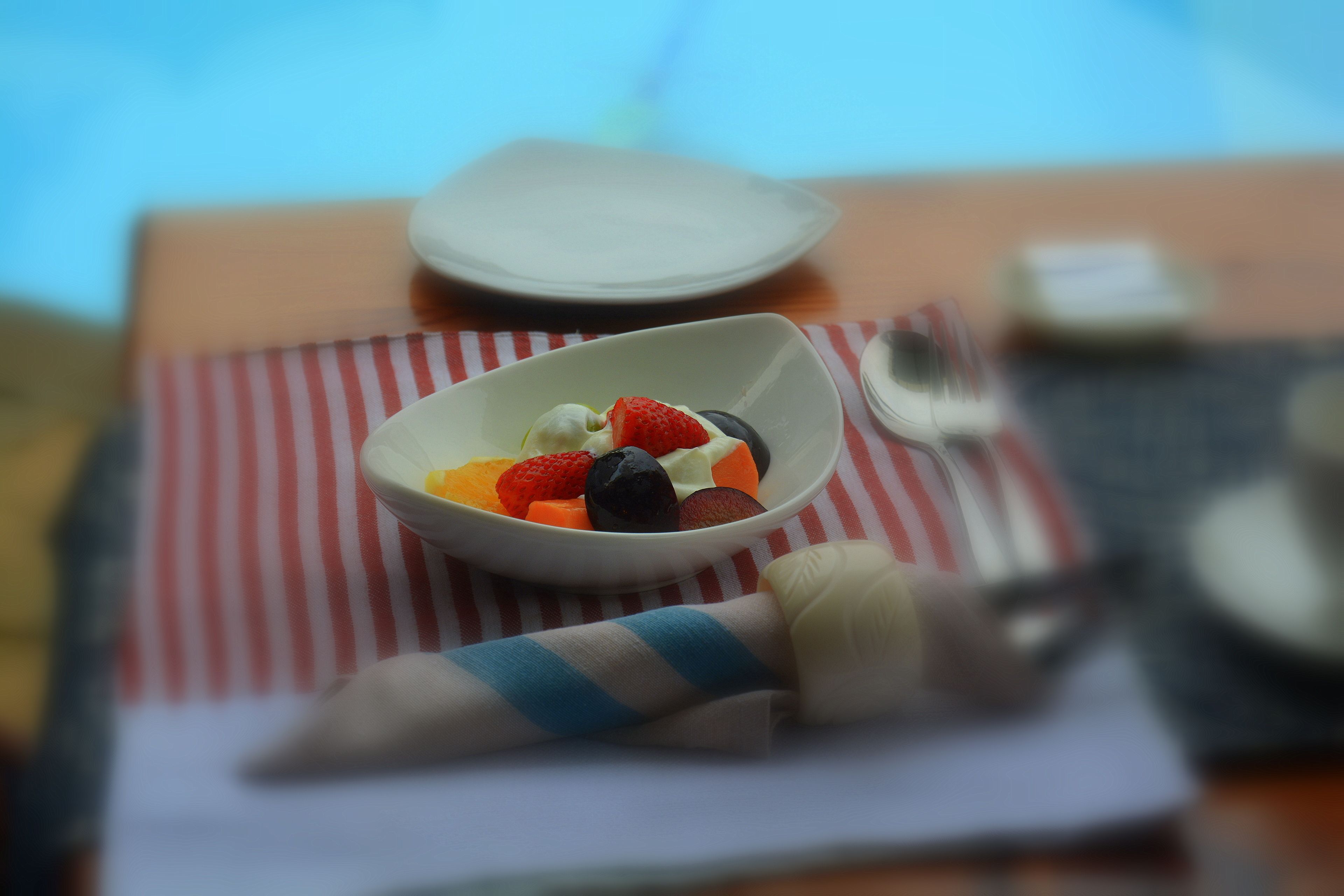 Un tazón de fruta sobre un mantel a rayas, con un tenedor y una servilleta a su lado.