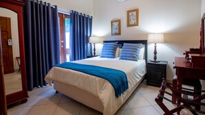 A bedroom with a bed, two bedside tables with lamps, a wooden chair, a mirror, and a door with curtains. - Turtle Bay Lodge (St. Lucia)