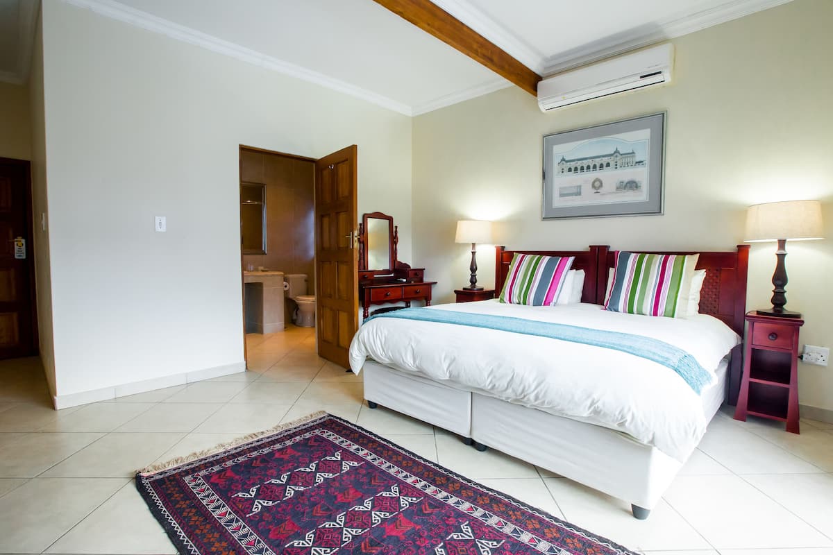 Quarto com uma cama grande, duas mesas de cabeceira, um criado-mudo, cabeceira de madeira, um quadro emoldurado na parede e um tapete estampado no chão.