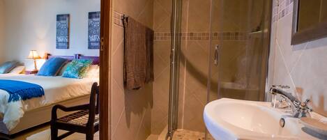 Una habitación de hotel con cama, una silla, ducha y lavamanos.