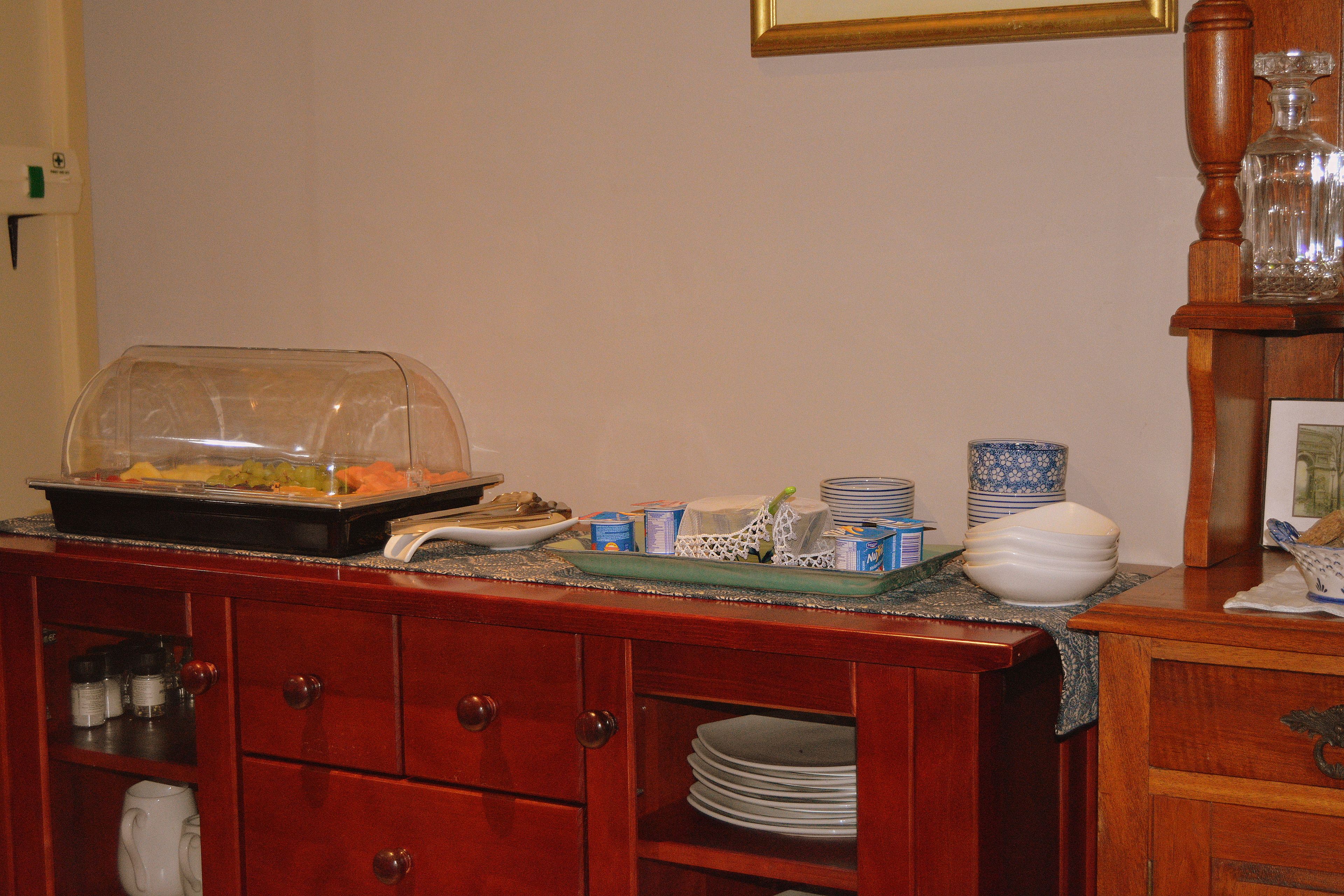 A buffet setup with a glass-covered food display, stacked plates, and a decorative vase.