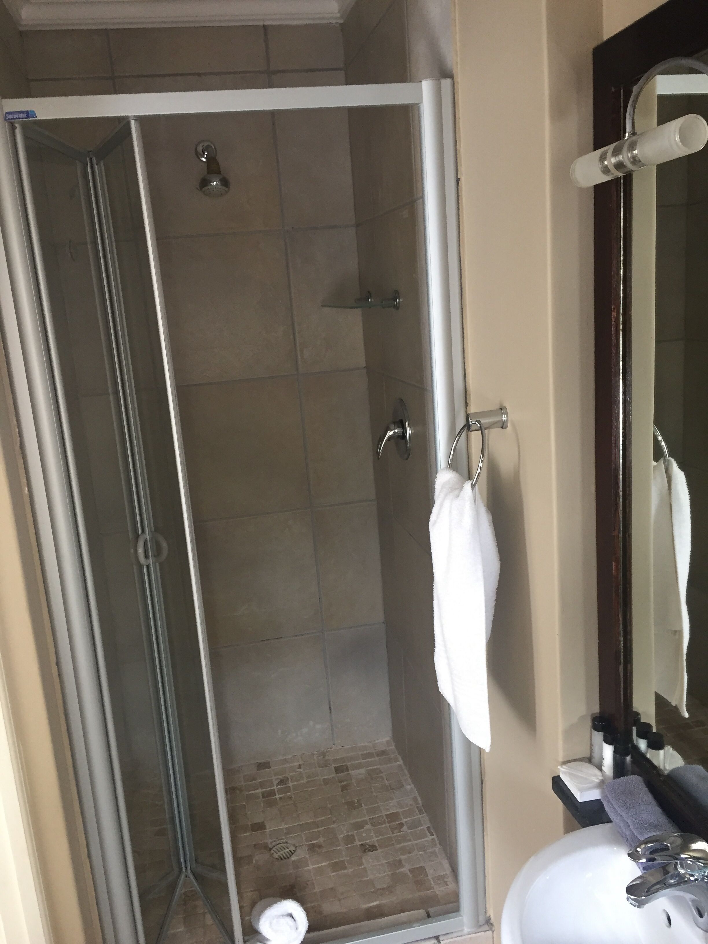 A shower with a glass door, a white towel hanging on a rack, and a sink with a mirror above it.
