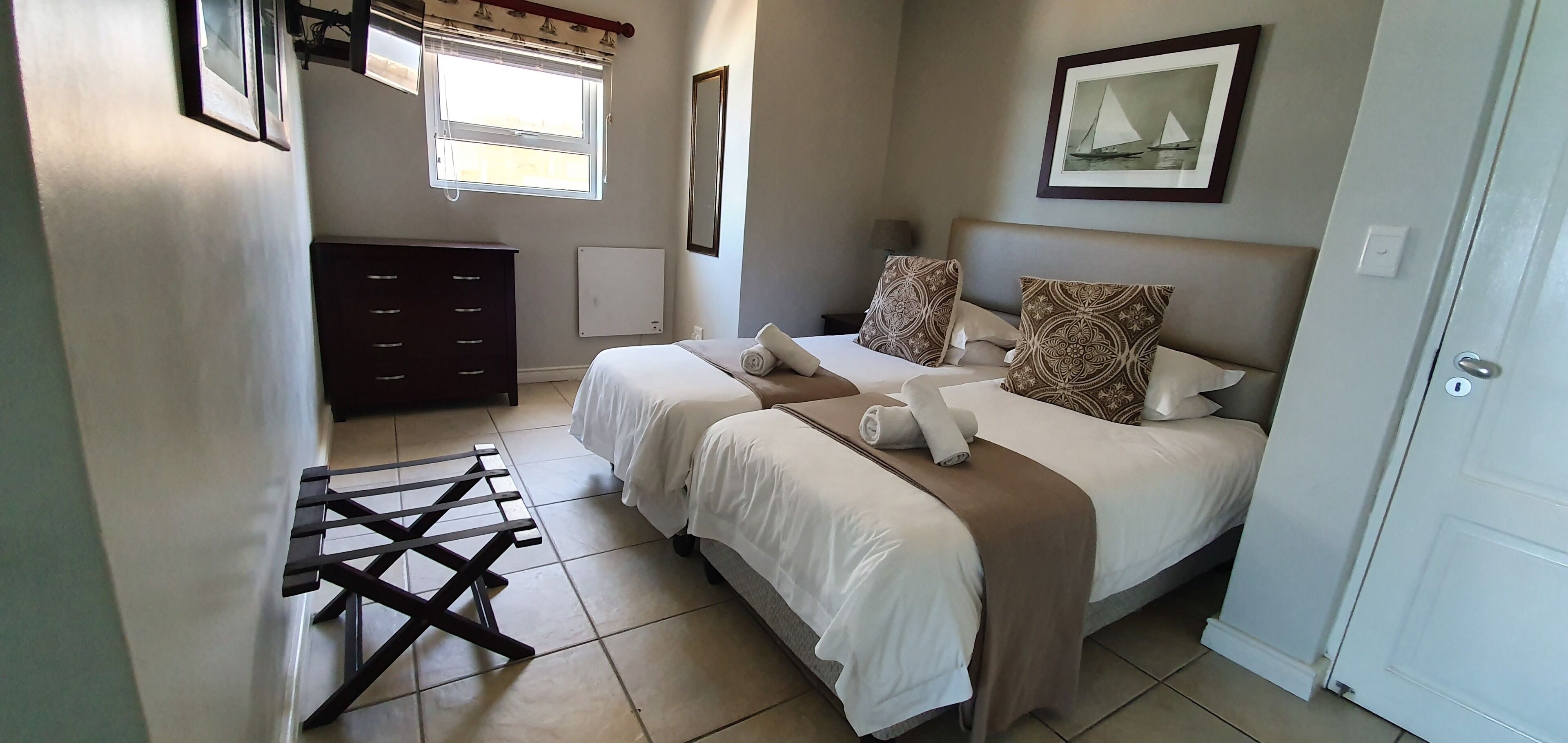 Une chambre d’hôtel avec deux lits, une commode, un radiateur et une fenêtre avec des rideaux.