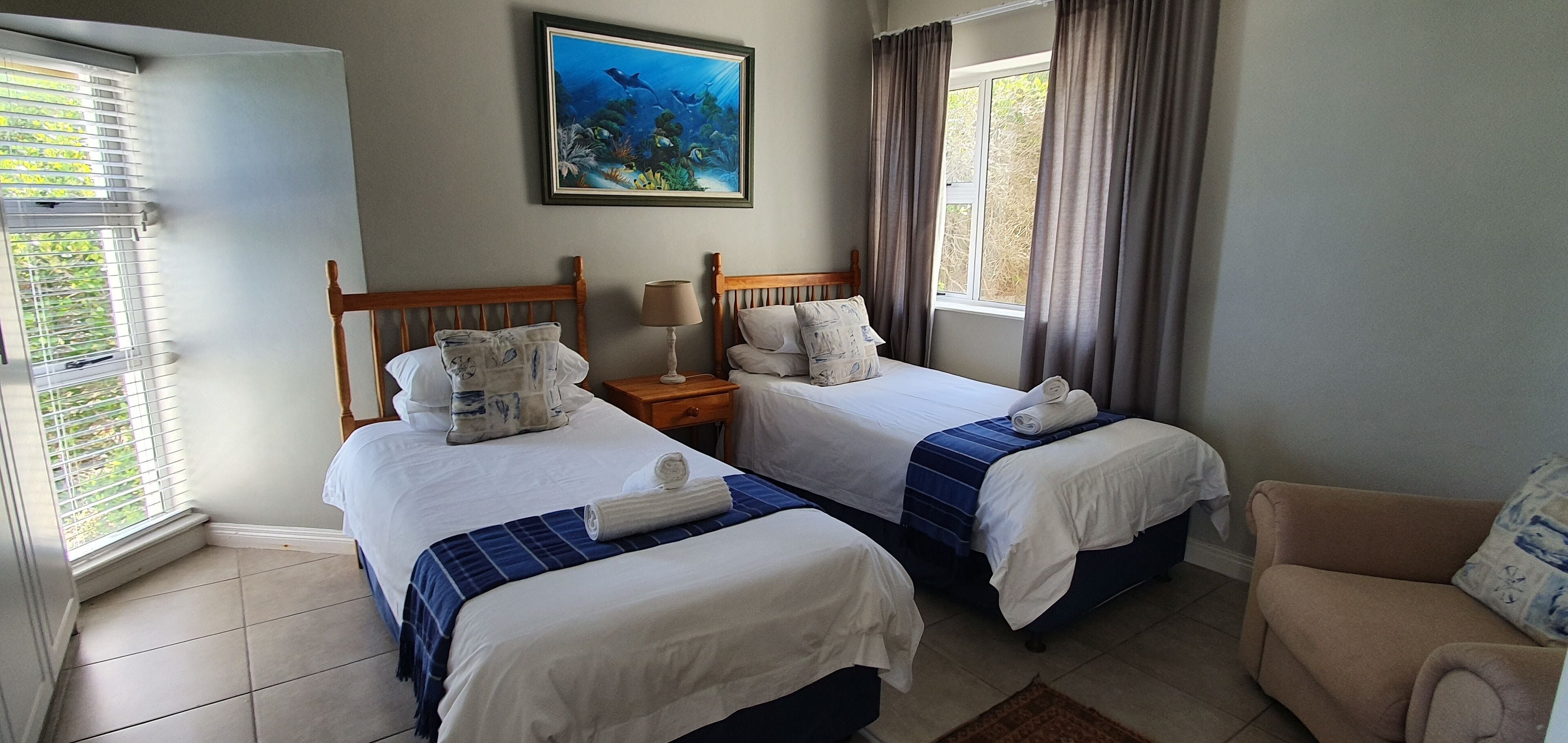A hotel room with two beds, a nightstand, a lamp, a painting, and a window with curtains.
