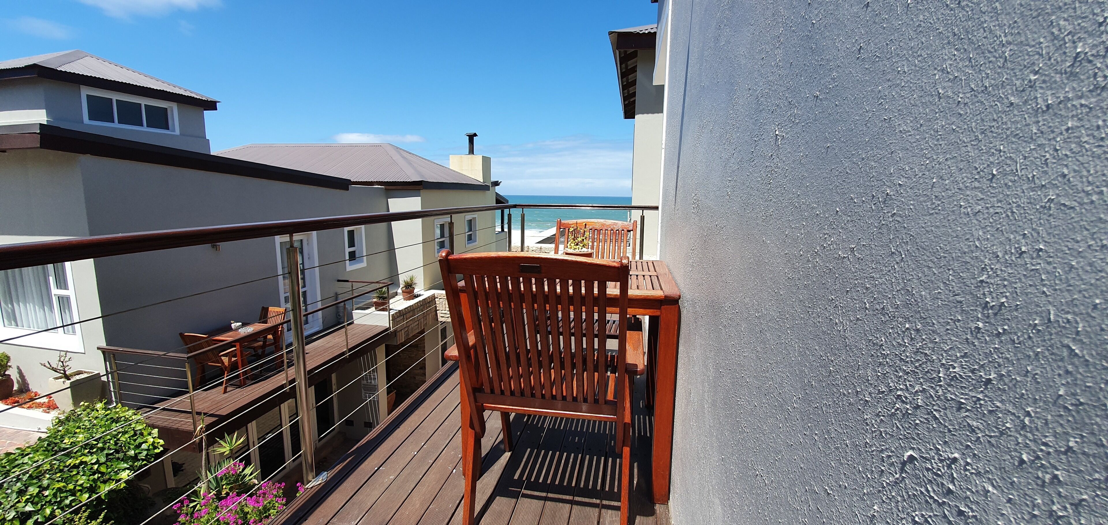 Un balcón con mobiliario de madera, vistas al mar y un edificio de fachada blanca.