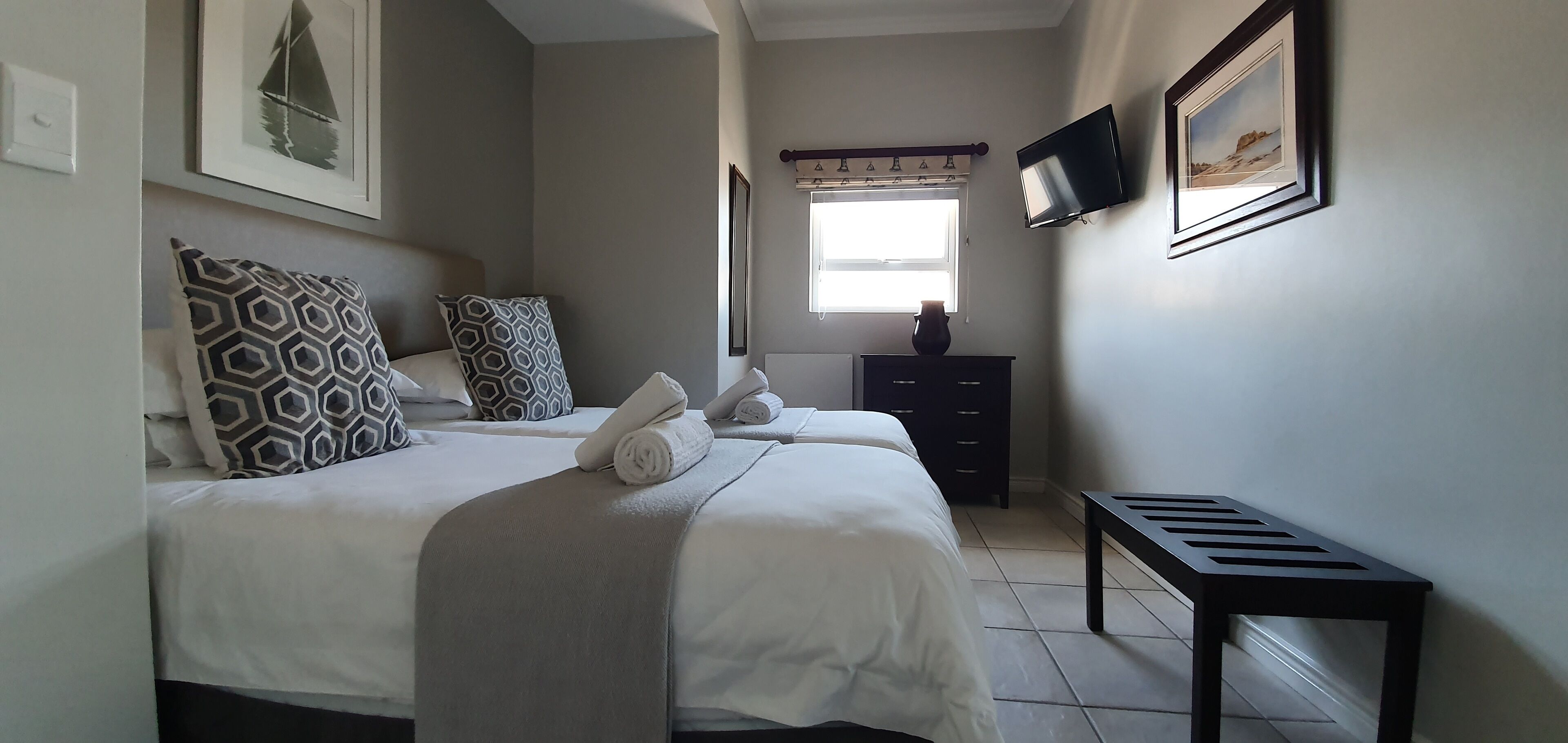 A bedroom with a bed, pillows, a dresser, a TV, and a window.