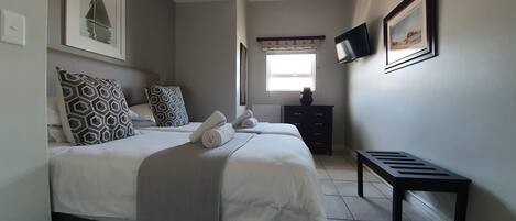 A bedroom with a bed, pillows, a dresser, a TV, and a window.