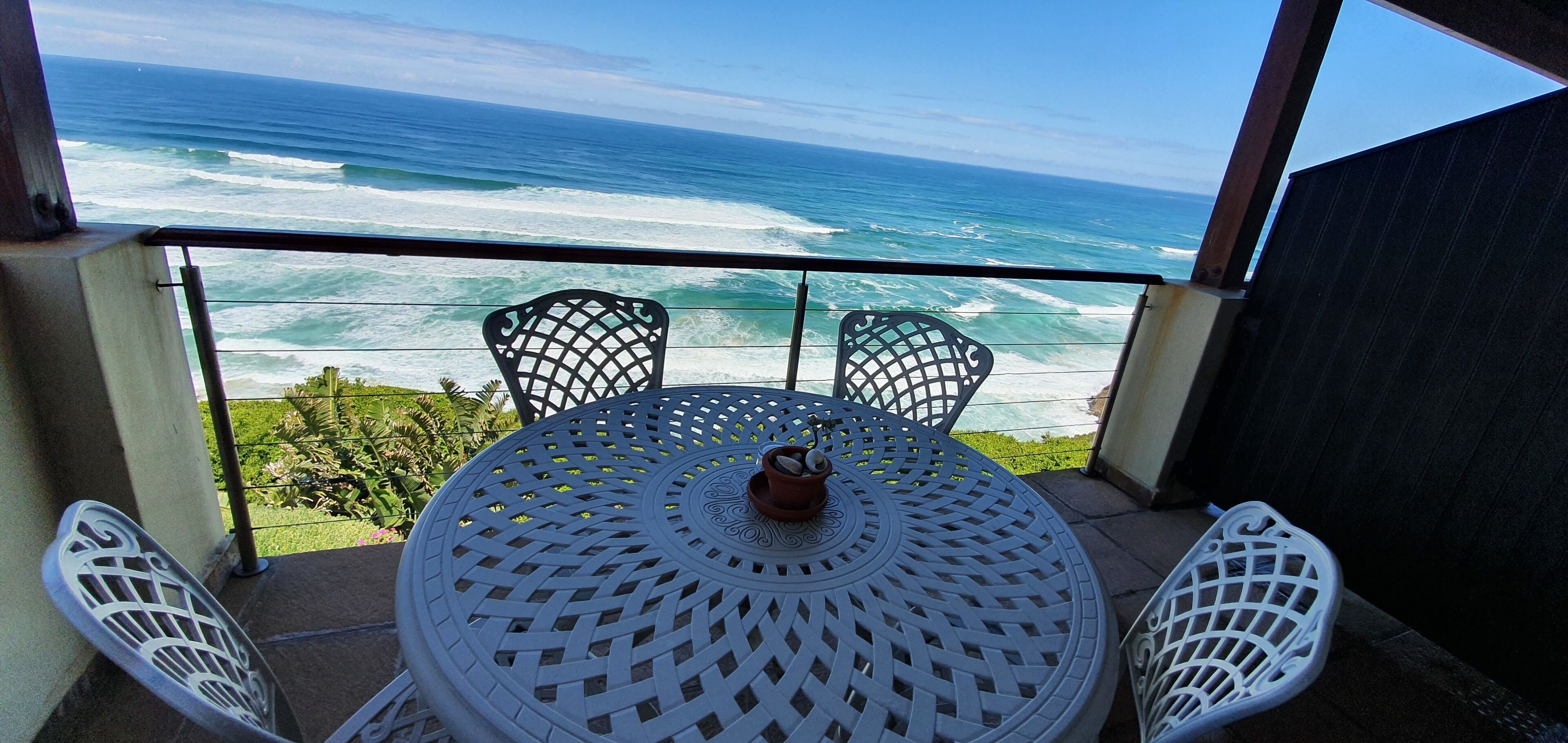 Ein Balkon mit rundem Tisch und zwei Stühlen mit Blick auf den Ozean.