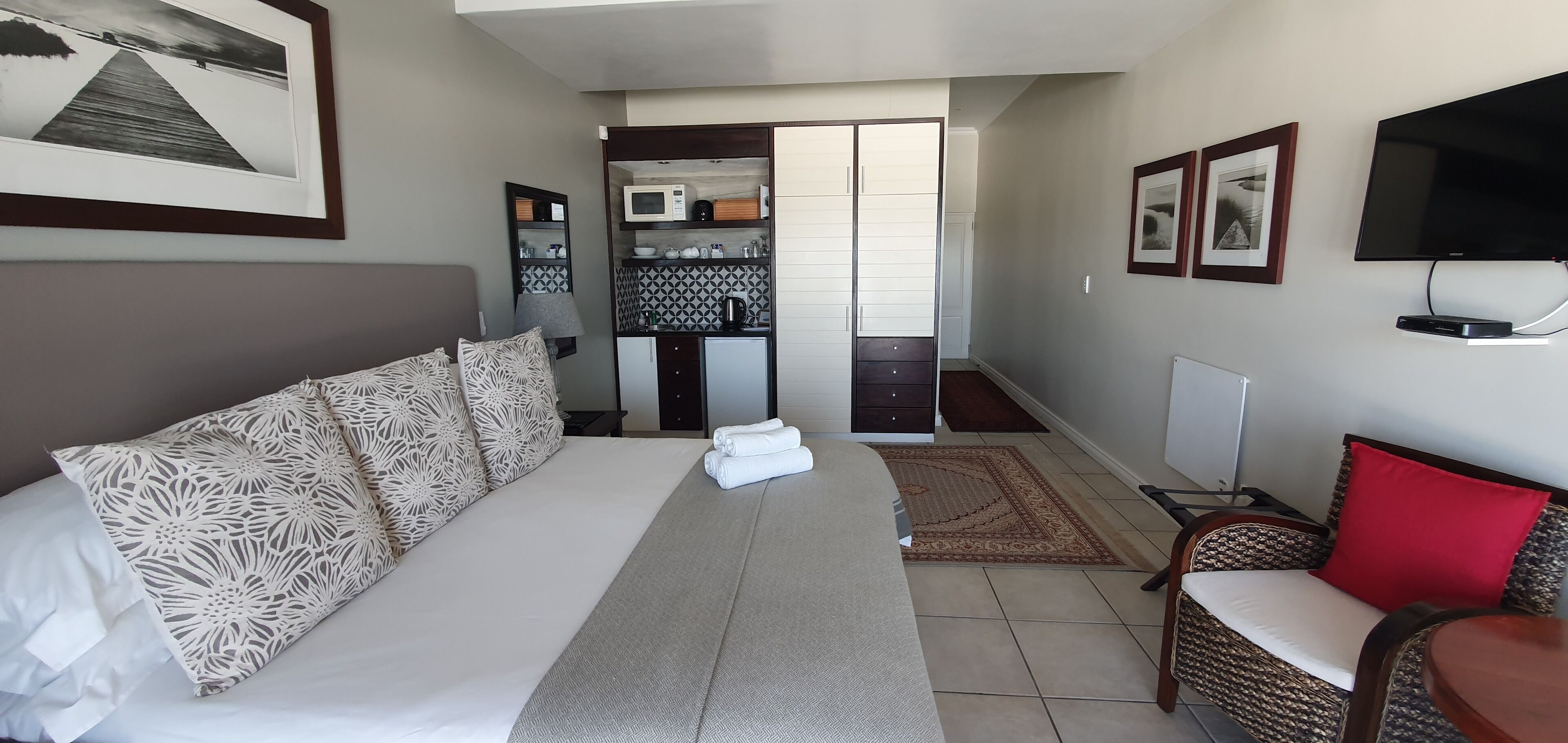 A hotel room with a bed, a chair, a TV, and a kitchenette.