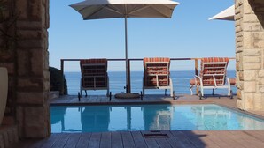 Un espace aménagé au bord de la piscine, avec deux chaises longues et un parasol, offrant une vue sur un ciel bleu et une eau cristalline.