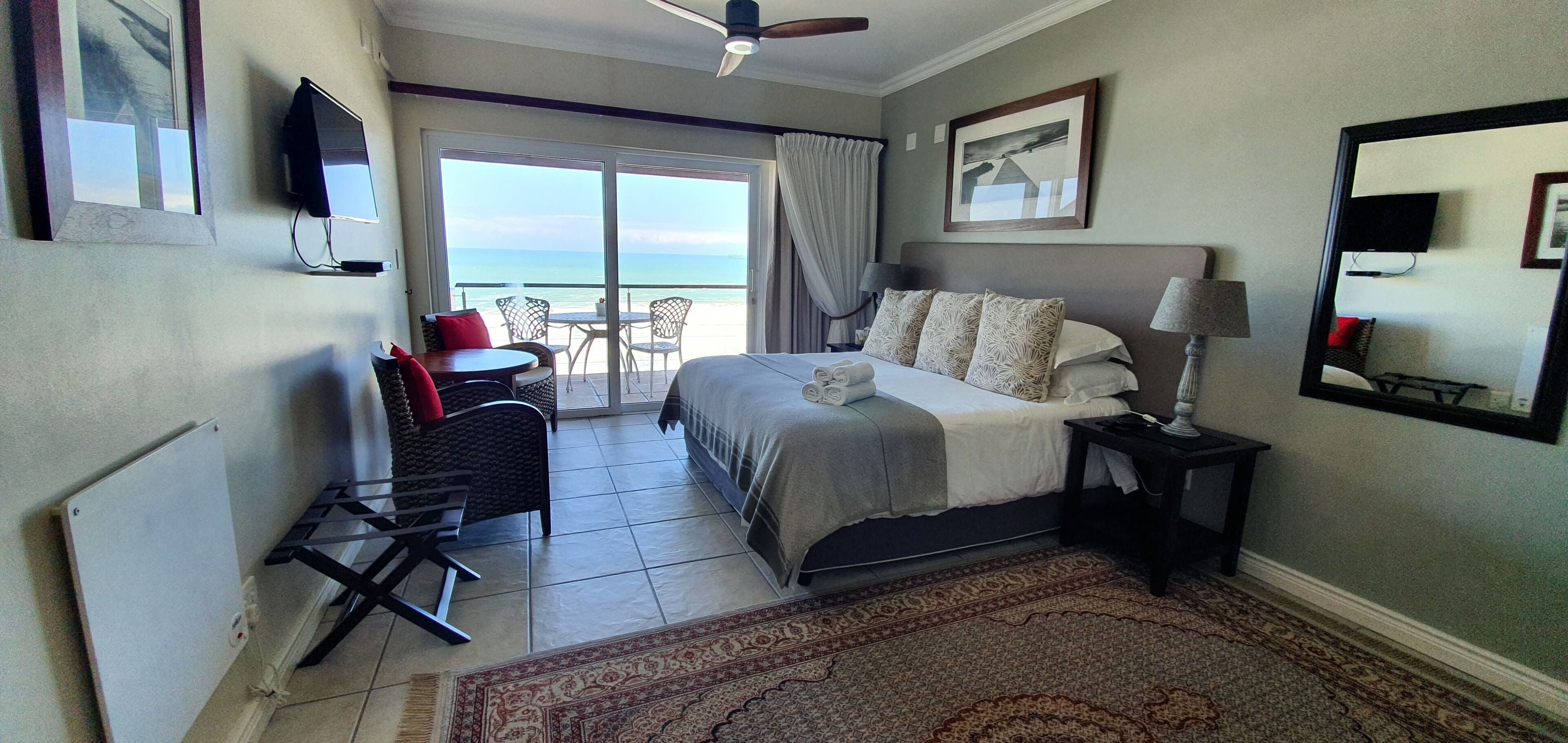 A hotel room with a bed, a desk, a chair, a TV, a lamp, and a view of the ocean through the sliding doors.