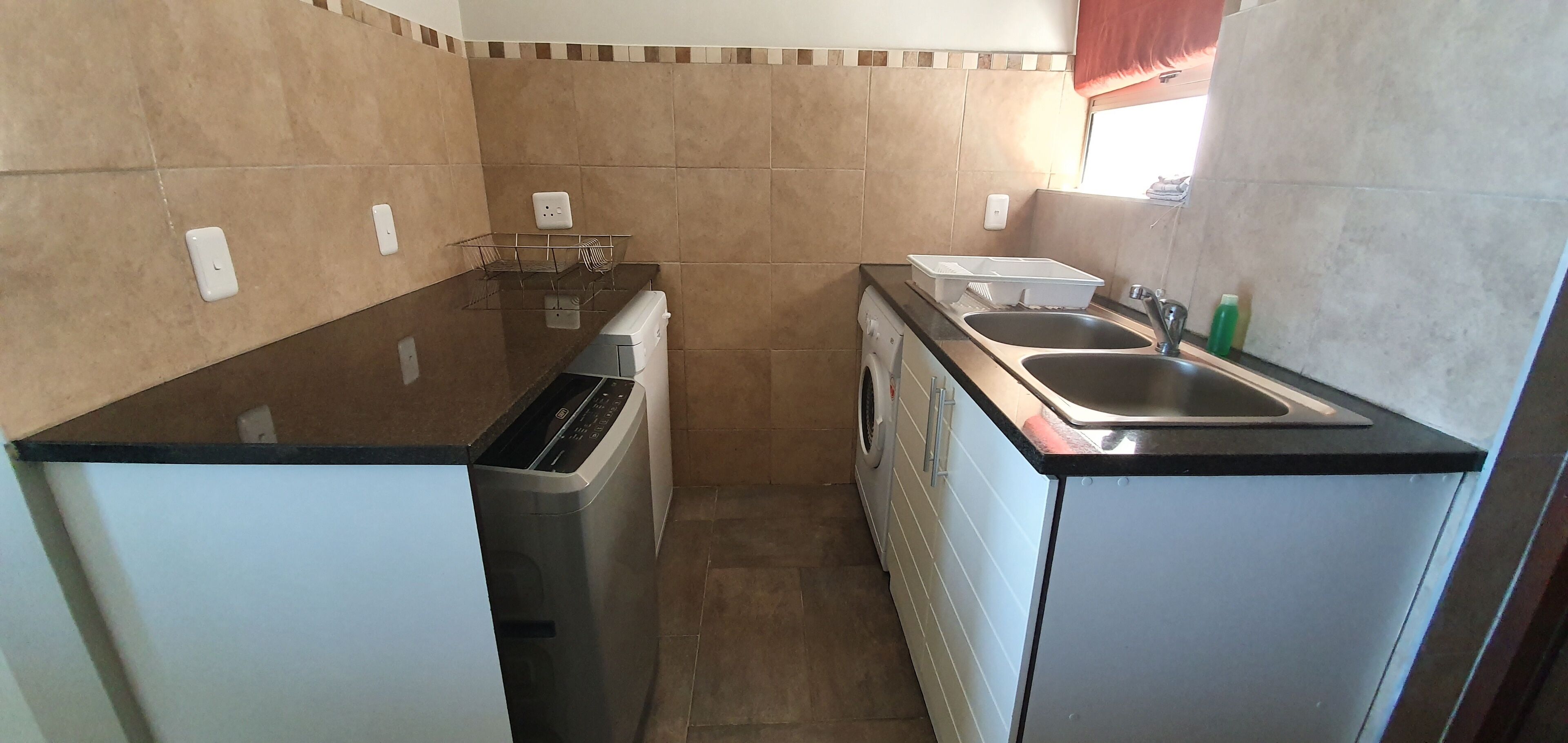 A compact kitchen with a dishwasher, washing machine, and a double sink.