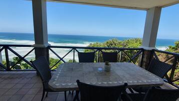 Uma área de estar coberta ao ar livre, com mesa e cadeiras, com vista para o oceano.
