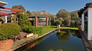 A serene garden with a pond, a pergola, and a mountain backdrop. - Brown Jug Guest House (Hermanus)