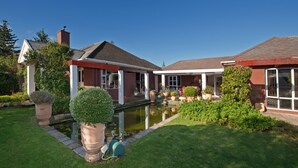 A house with a pond, surrounded by well-maintained lawns and potted plants. - Brown Jug Guest House (Hermanus)