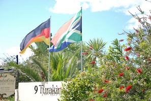 Une enseigne indiquant « 9 Turakina », avec deux drapeaux, un palmier et des fleurs rouges.