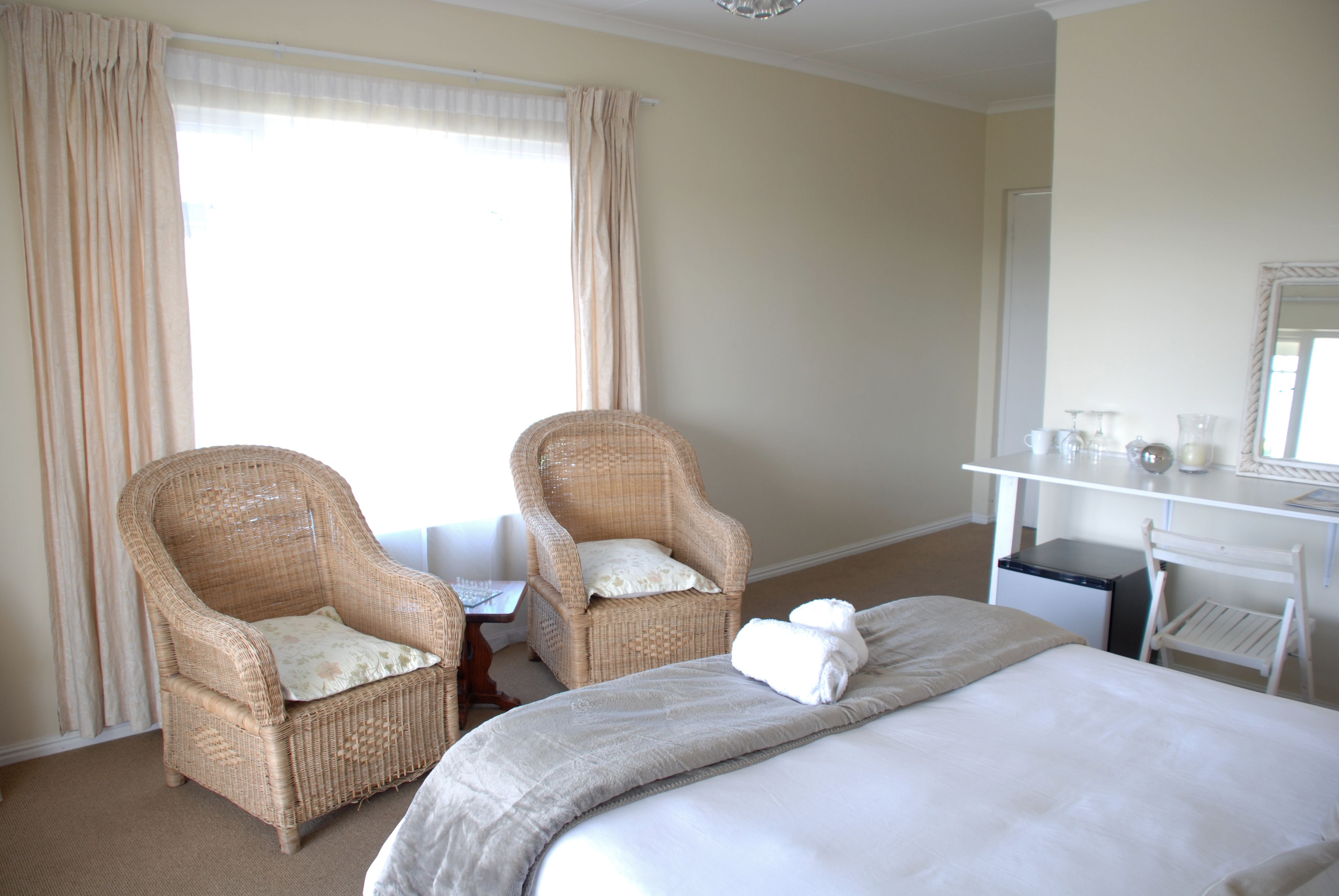 A hotel room with a large bed, two wicker chairs, a desk with a computer, and a mirror.
