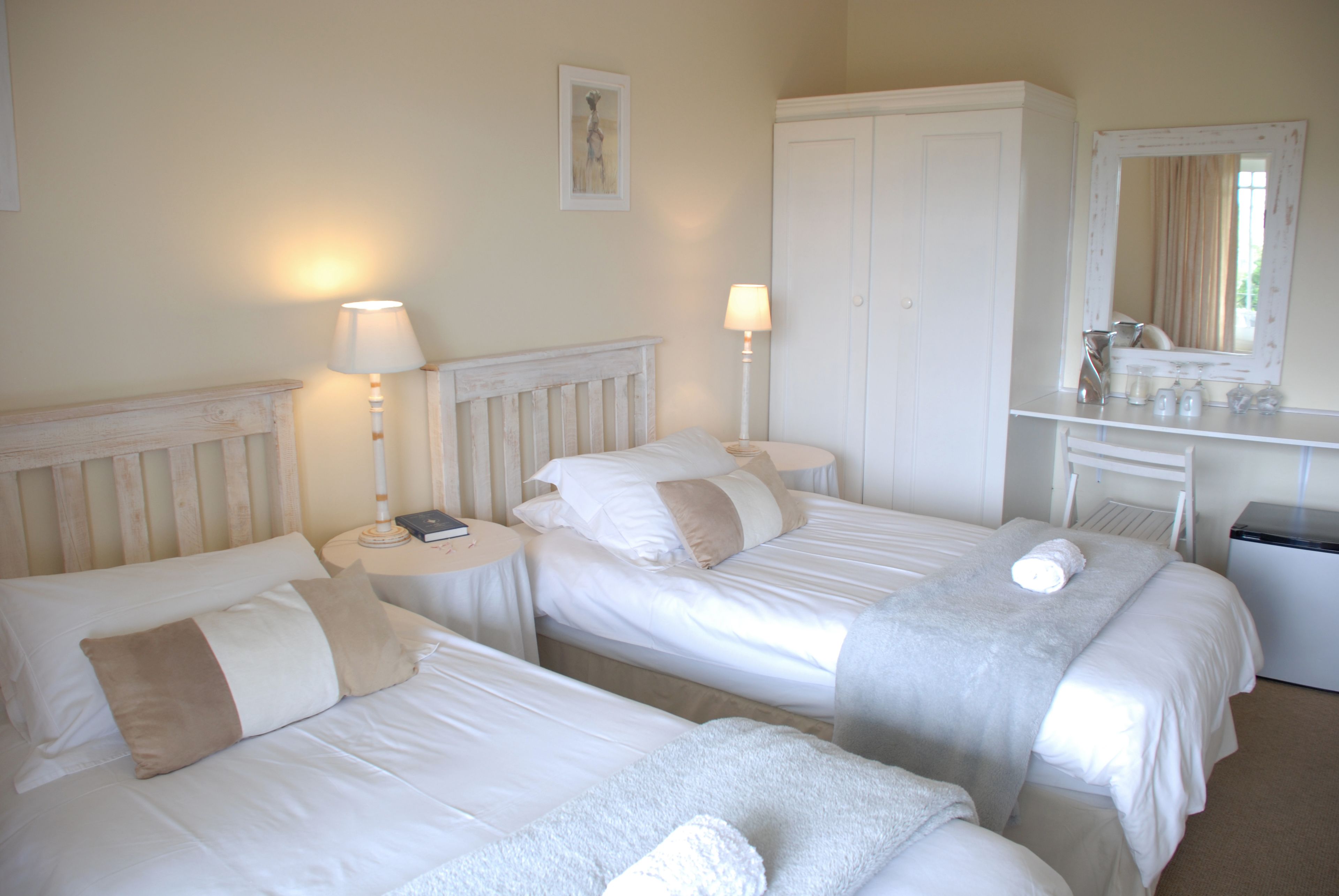 A hotel room with two single beds, bedside tables with lamps, a wardrobe, and a mirror.