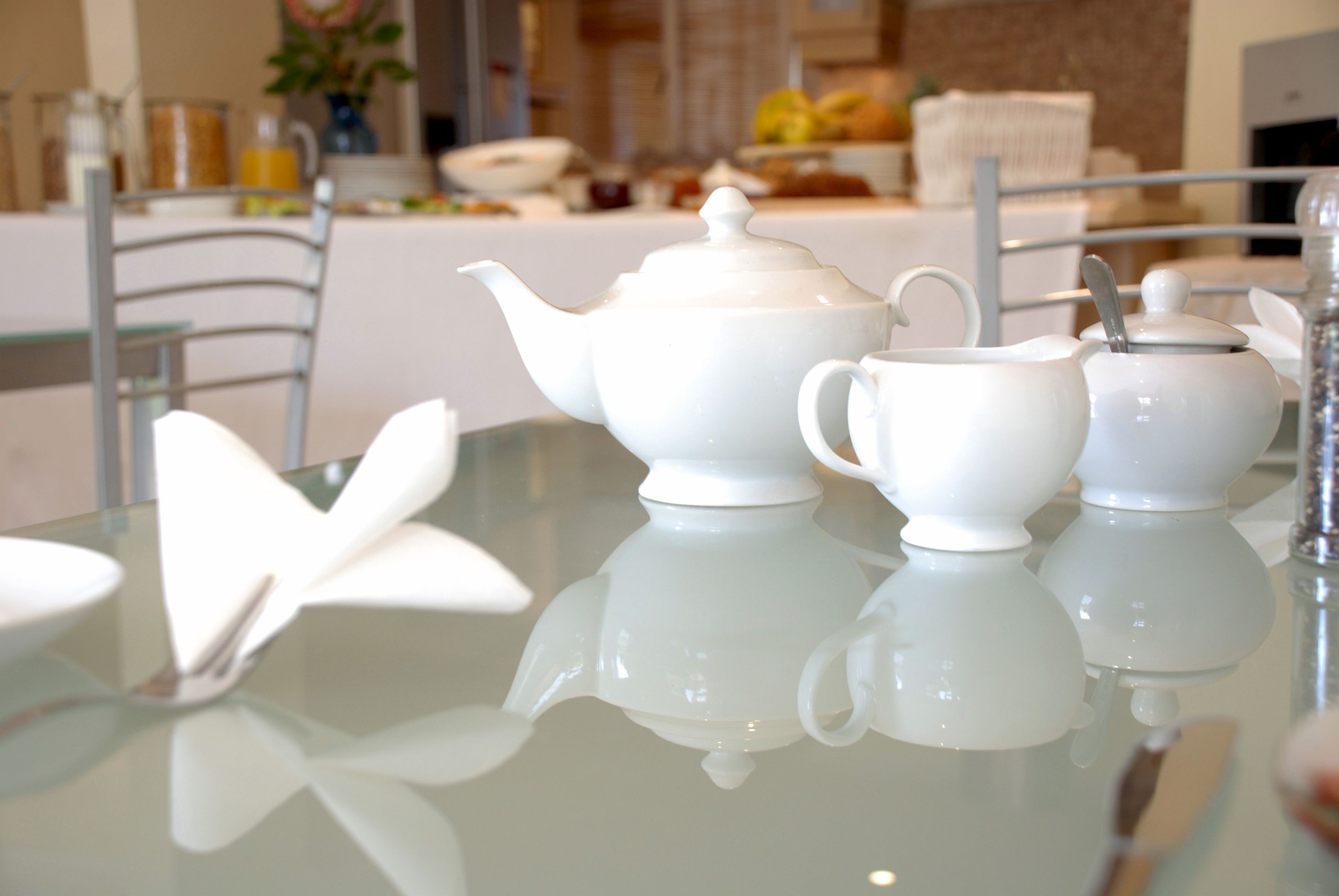 A table with white teapots and a teapot lid, a white butterfly-shaped object, and a glass table.
