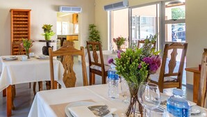 A dining area with wooden chairs and tables, a wooden bookshelf, and a window with a view. - Sabie Retreats Guest House (Sabie)