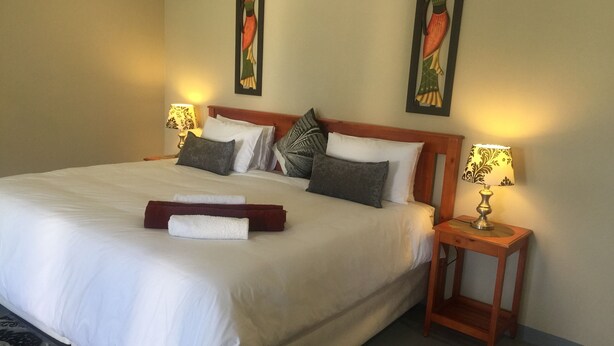 A neatly made bed with white linens, a wooden headboard, and two bedside tables with lamps. - Sabie Retreats Guest House (Sabie)