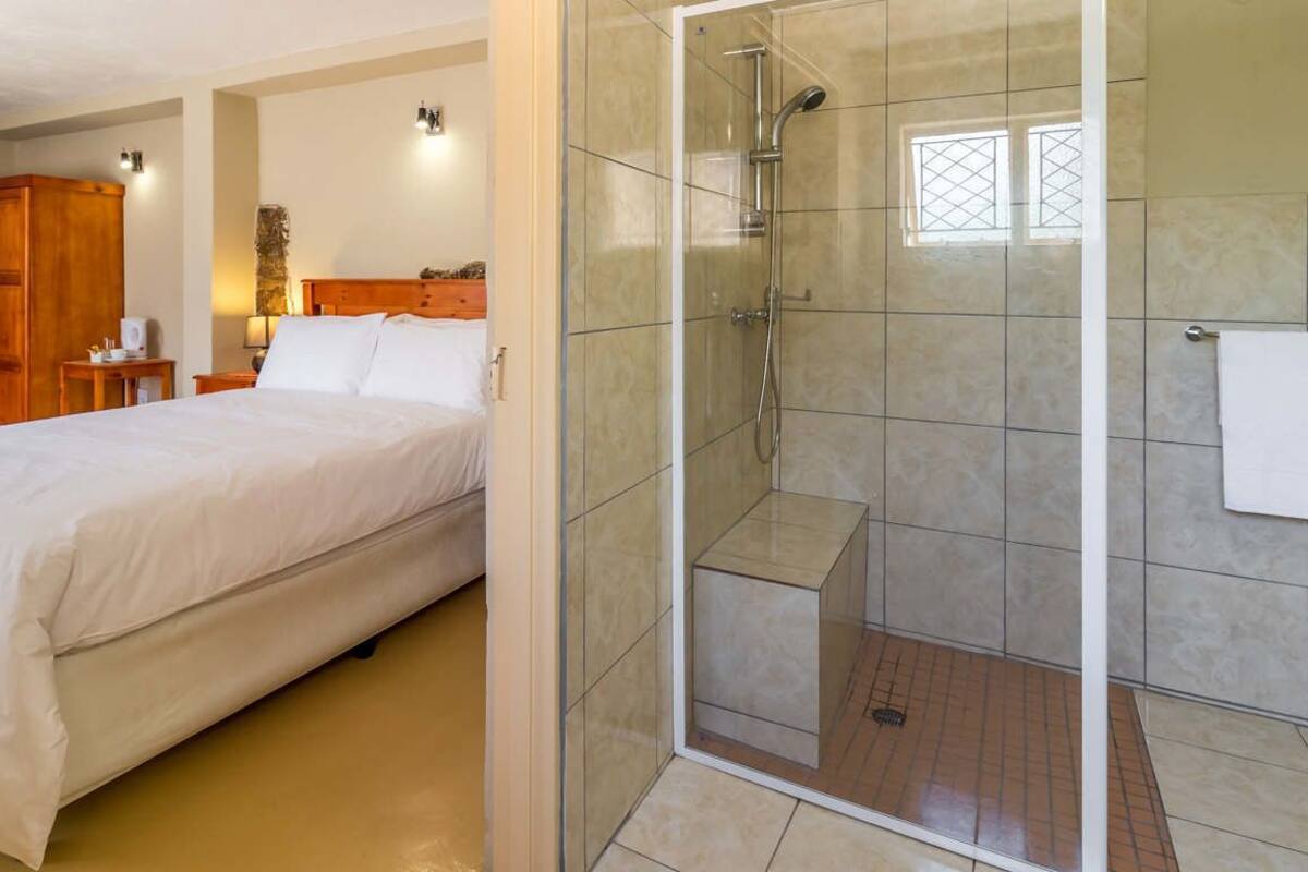 A bedroom with a bed, a wooden wardrobe, a nightstand, and a bathroom with a glass-enclosed shower.