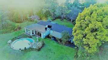 A large house with a swimming pool, surrounded by lush greenery and trees.