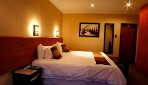 Habitación de hotel con una cama grande, una mesita de noche, una lámpara de pared y un cuadro en la pared.