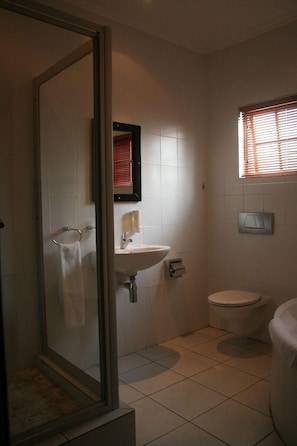 Un baño con cabina de ducha de vidrio, lavabo, inodoro y ventana con persianas.