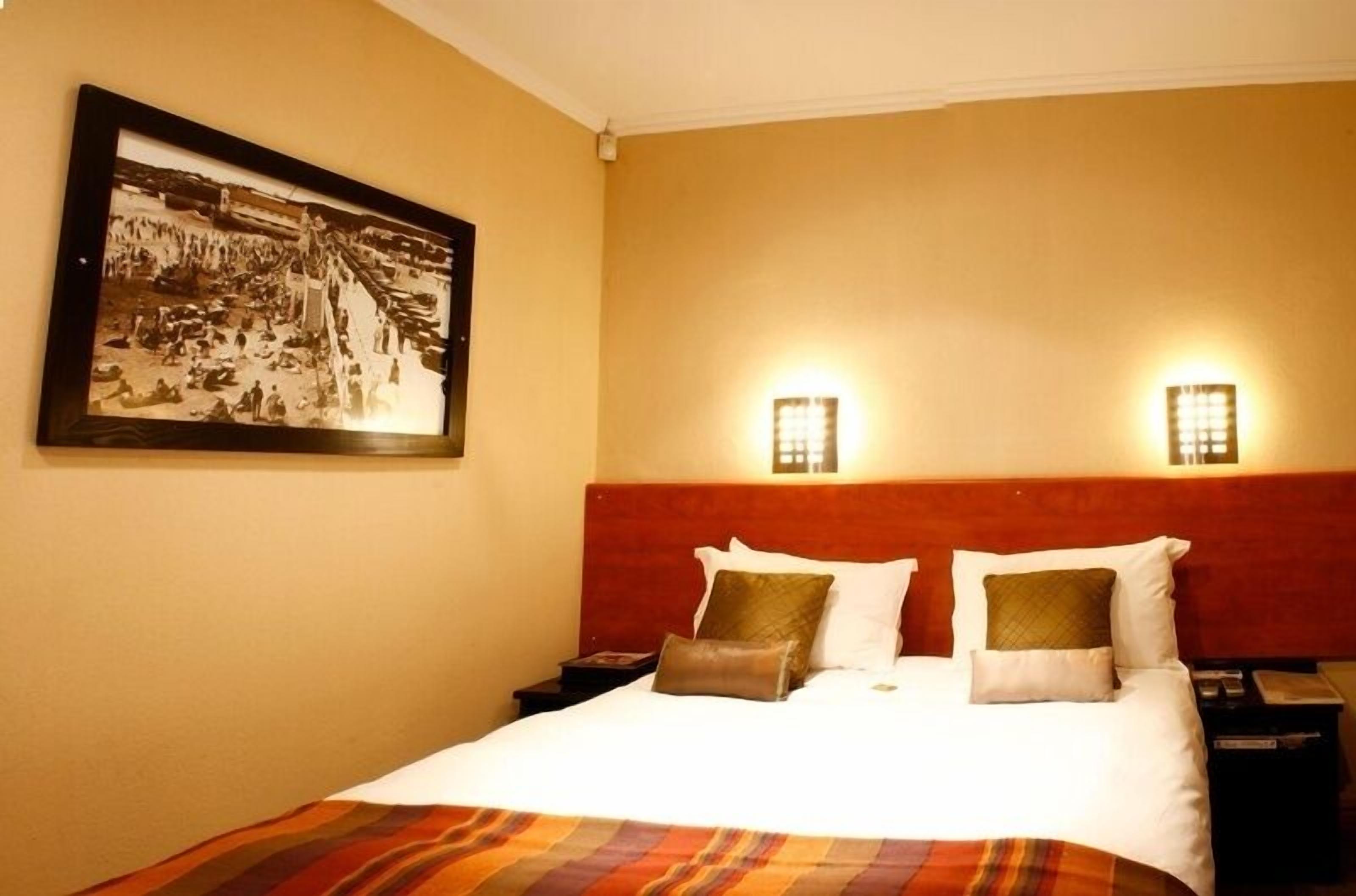 A hotel room with a bed, two bedside tables, a headboard, and two wall-mounted lights.