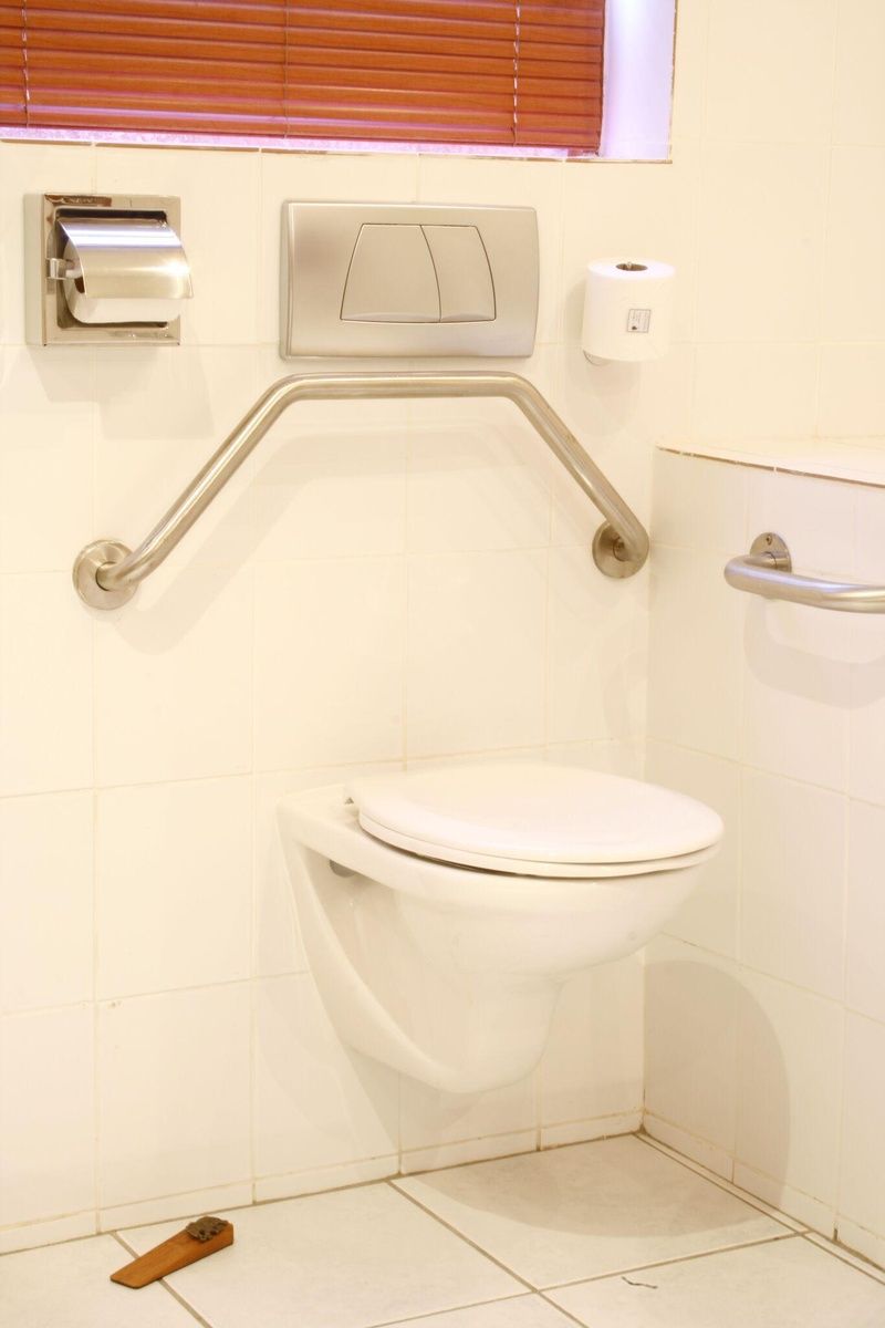 Et badeværelse med et hvidt toilet, en håndtørrer og en papirhåndklædedispenser.