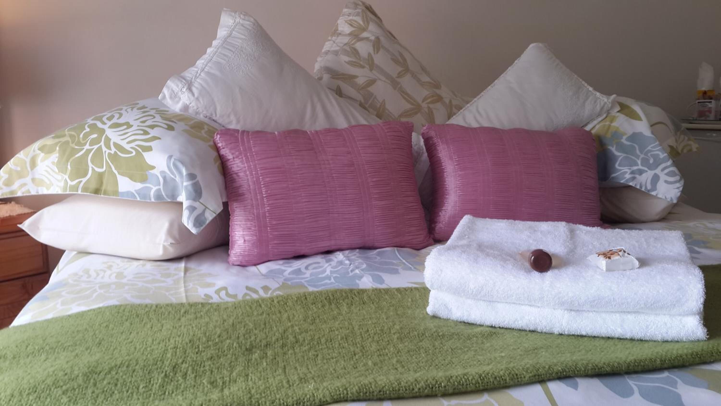 A bed with multiple pillows, a green throw blanket, and a folded white towel with a brown object on it.